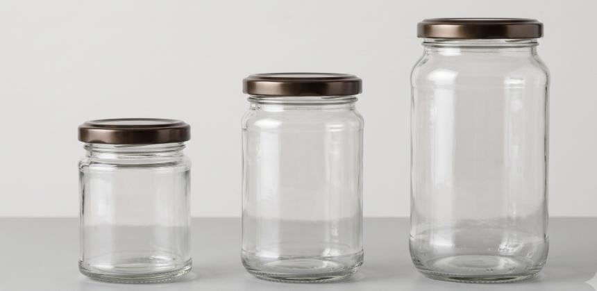 Three glass chutney jars in small, medium, and large sizes with metal lids, side by side on a plain background