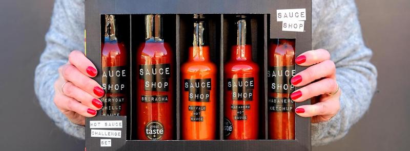 Woman holding a set of 5 bottles of hot sauces by sauce shop packed in a box